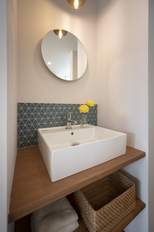 四角い洗面ボールと丸いミラー、三角のタイルが貼ってある写真。