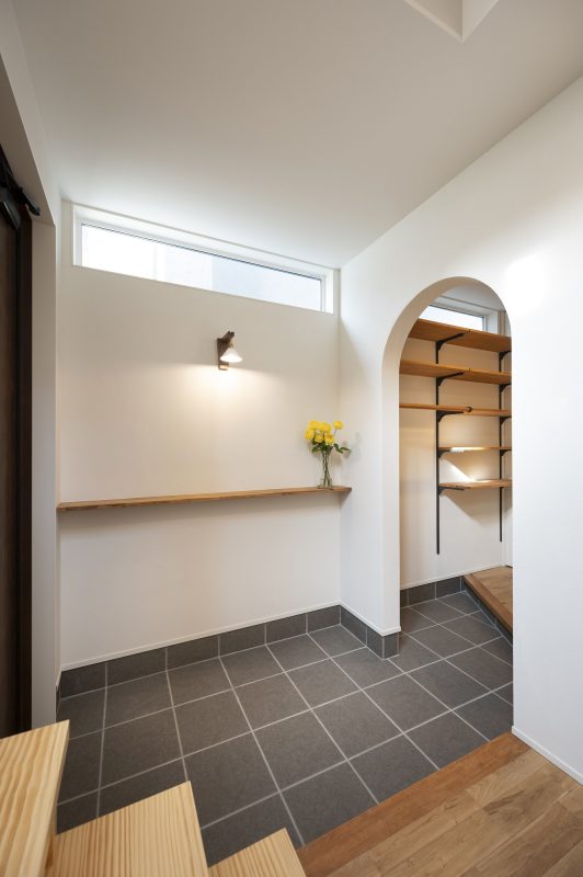 玄関土間に飾り棚があり、その上にかわいいブラケットの照明器具が優しい光を照らしている写真