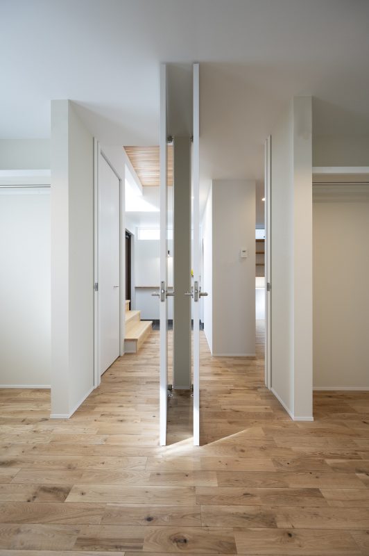 木のフロアとドアが2つ。その向こうに玄関土間が見える写真