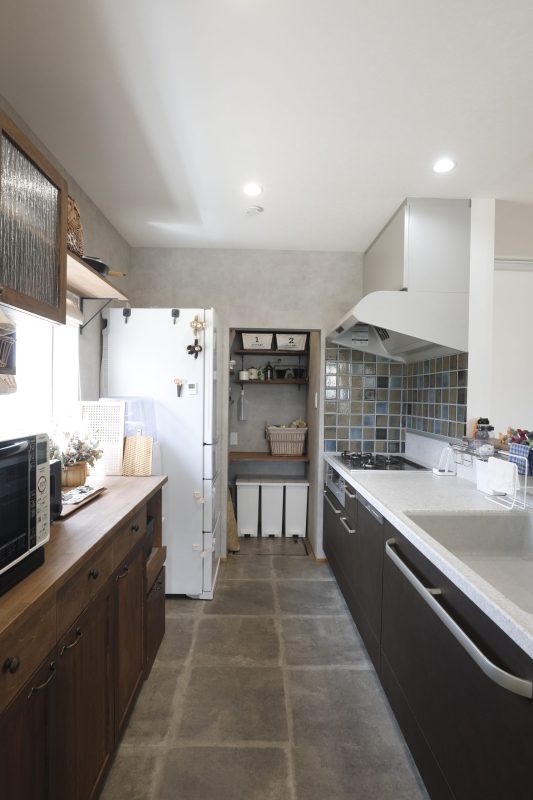 石目調のタイルフロアが貼ってあるキッチン。後ろには造作のキッチンバックがある写真