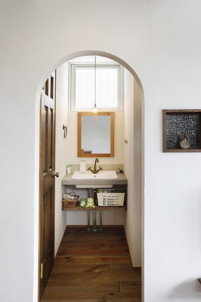 アーチの垂れ壁をくぐると木の枠で作ったミラーがある洗面台の写真