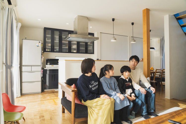４人家族がリビングのソファに座って談笑している様子